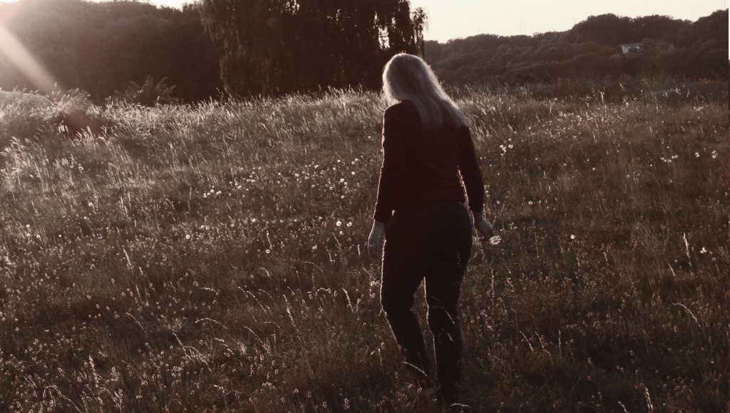 Janine Hofeditz, die über eine Wildblumenwiese im Abendlicht geht.